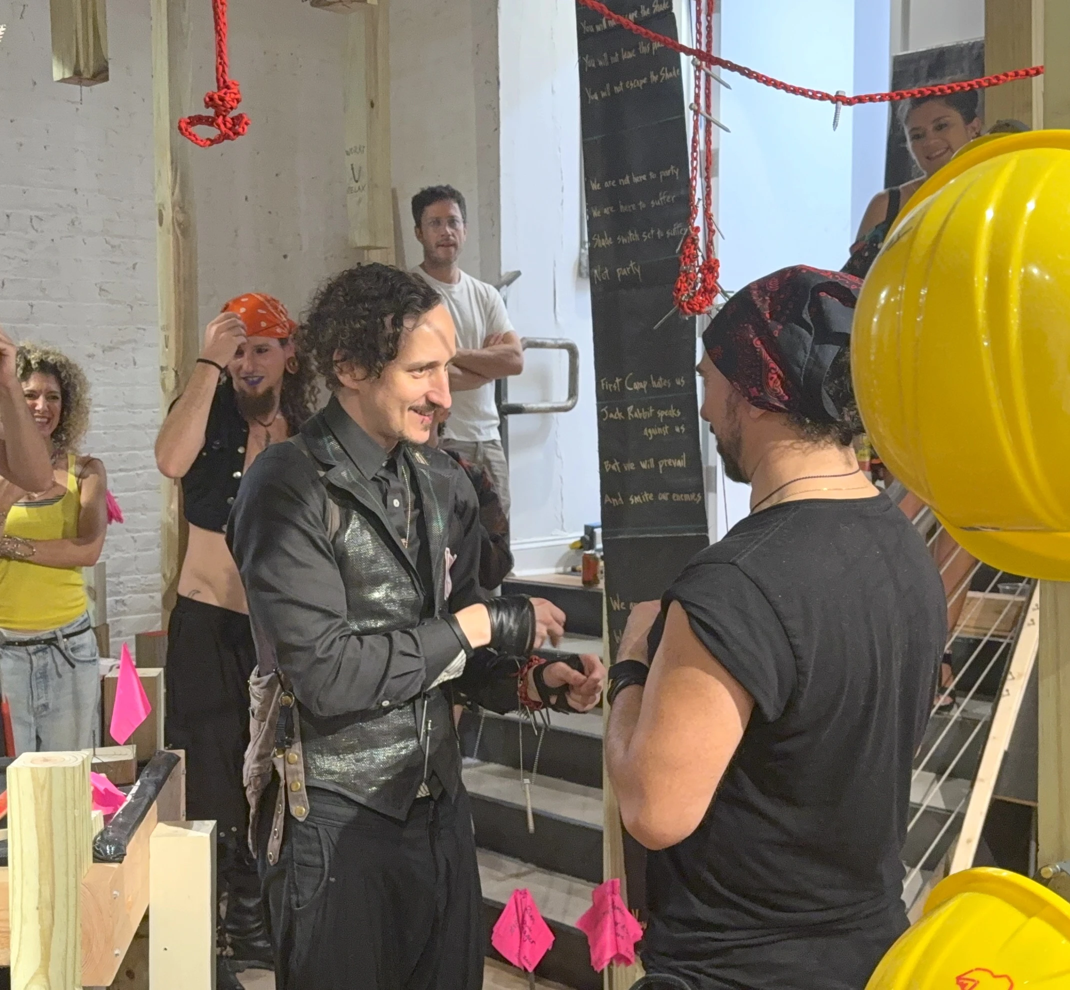 Artist Ian Henderson (left) bestows a badassner pendant on a Shade colleague during an activation of "Shenclave Actual" at The Ritual Division, July 2026