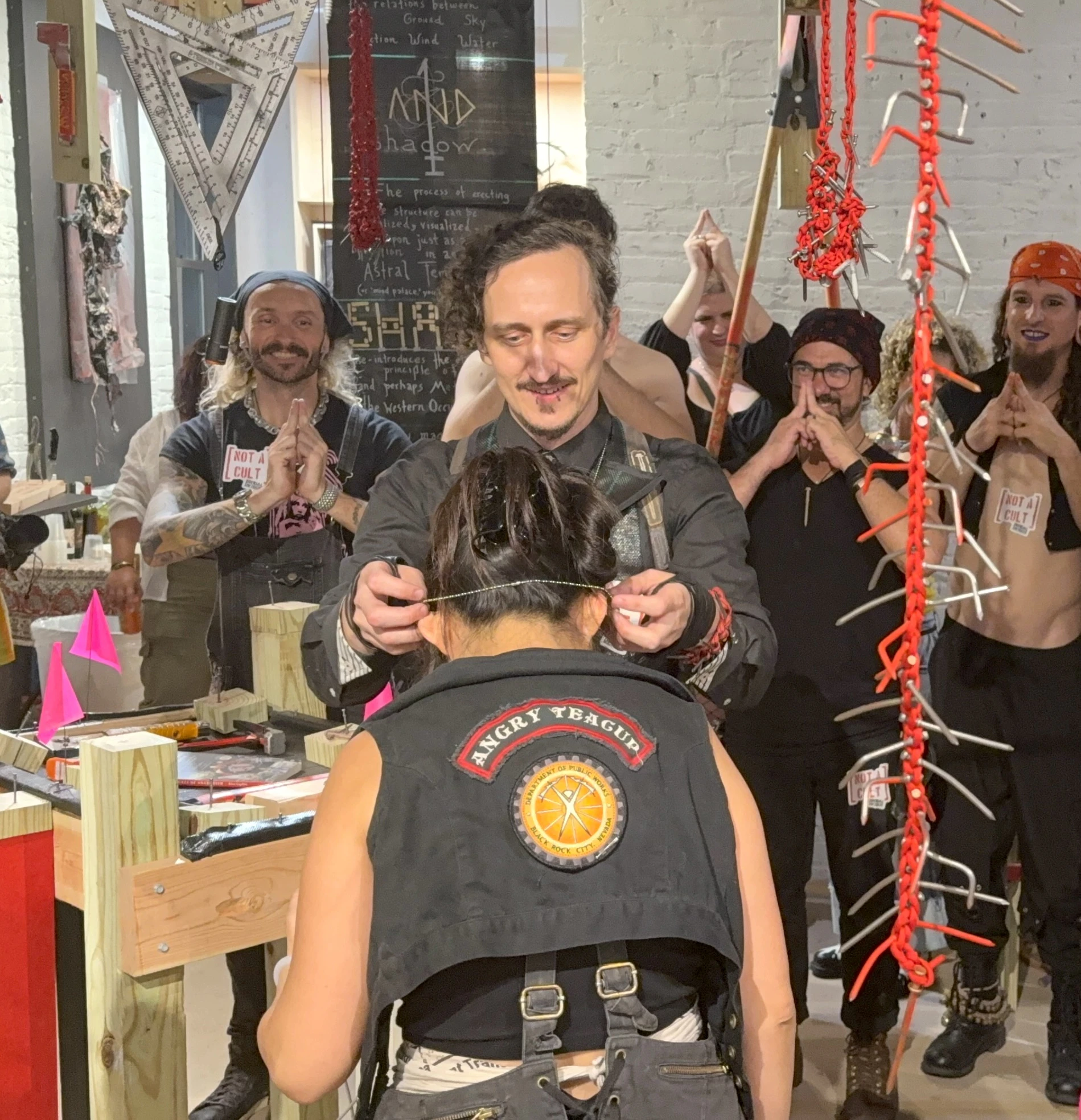 Artist Ian Henderson bestows a badassner pendant on a Shade colleague during an activation of "Shenclave Actual" at The Ritual Division, July 2026