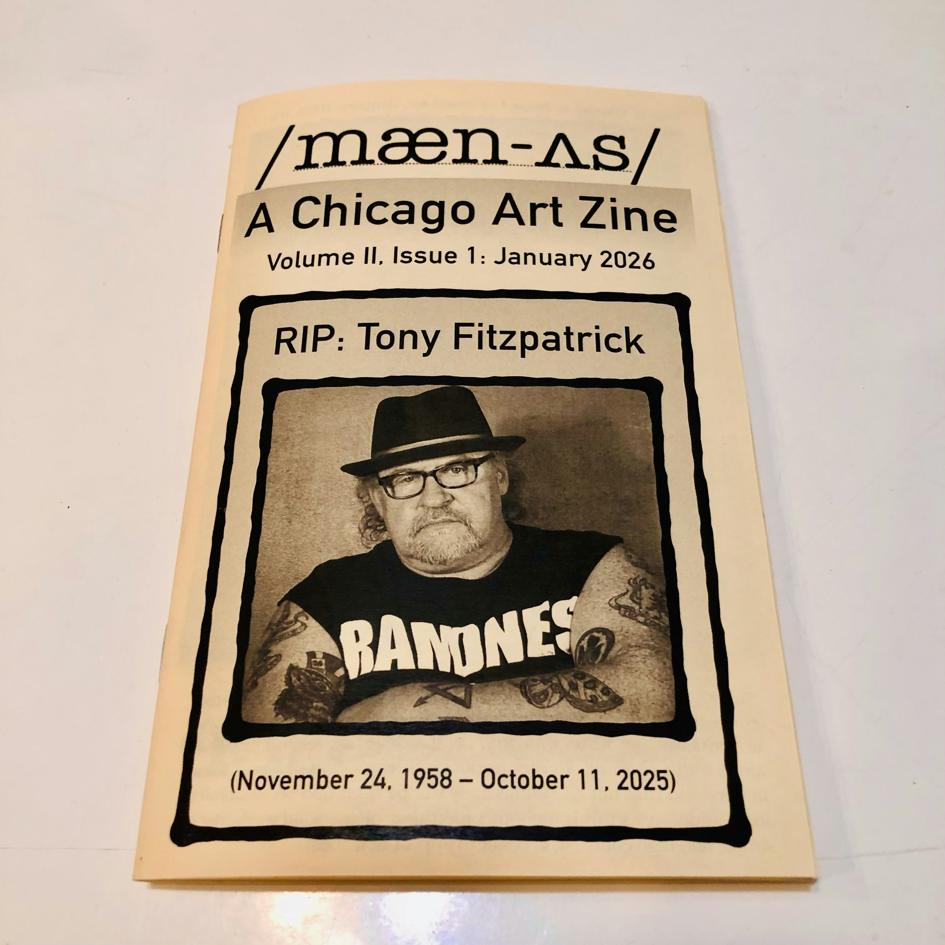 Image shows cover of /mæn-ʌs/ Chicago Art Zine Volume II, Issue 1: January 2026, which shows Chicago artist Tony Fitzpatrick with crossed arms, wearing a Ramones tee shirt, with the dates of his life underneath