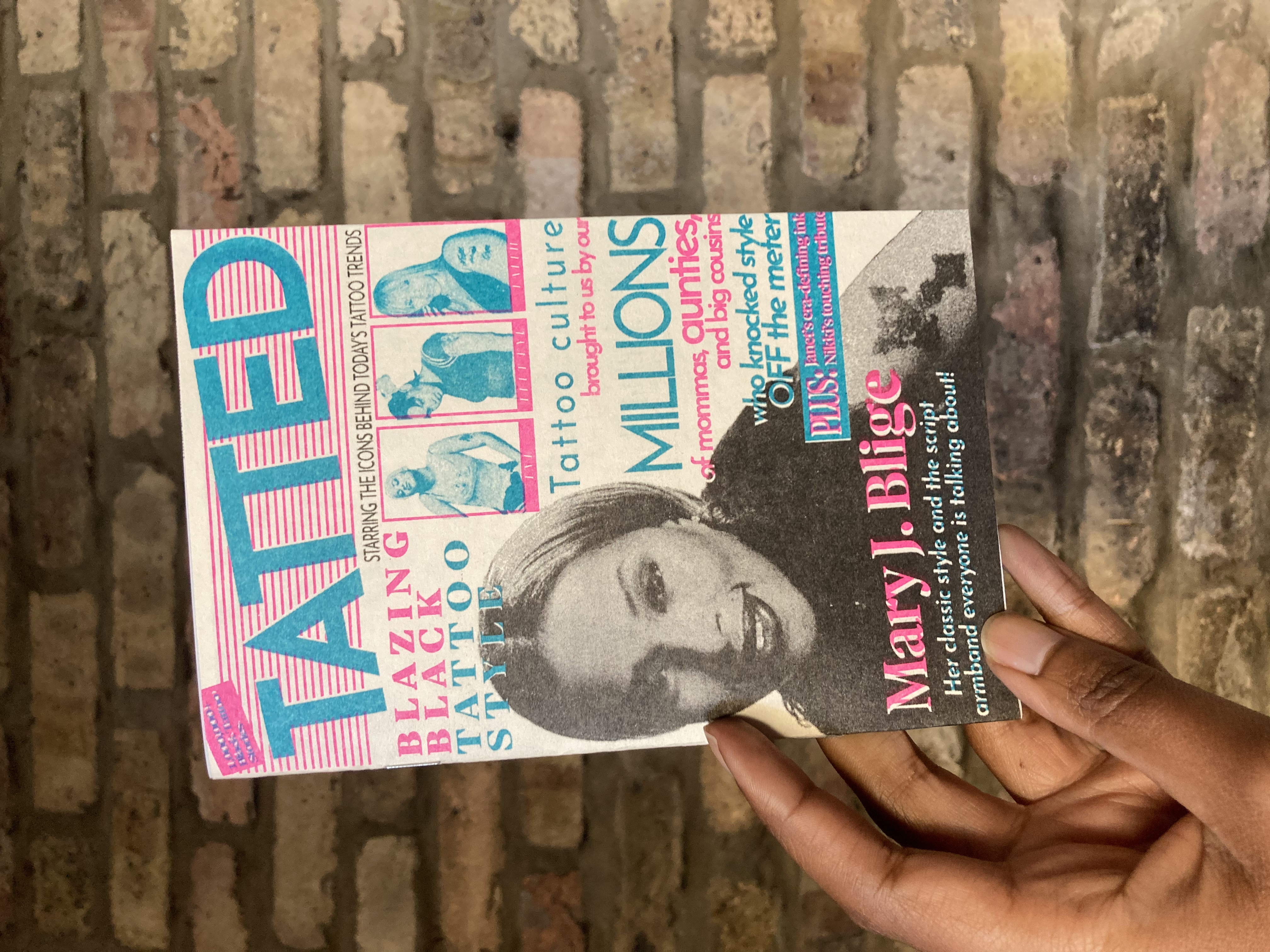 A blue pink and black cover of a mini magazine called Tatted featuring a headshot of Mary J. Blige showing a cross tattoo on her arm