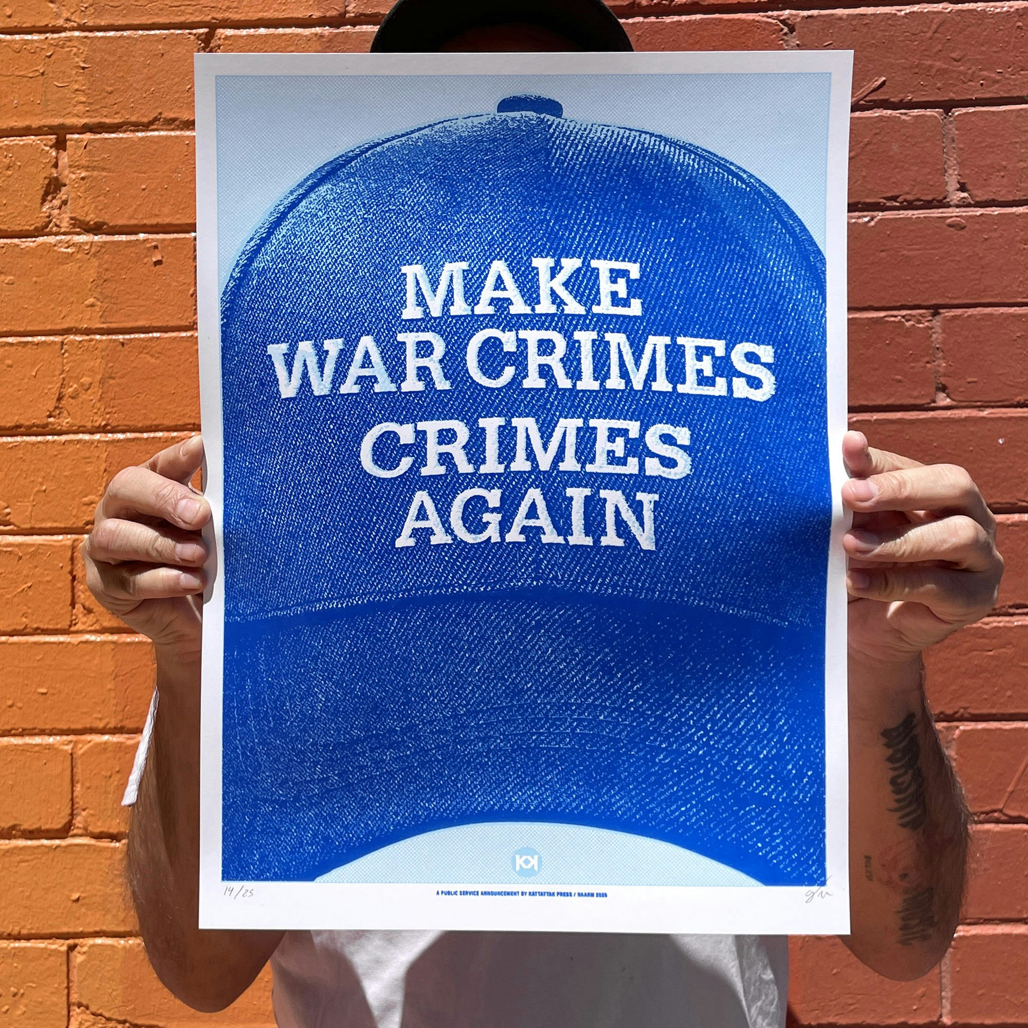Photography of a person holding an A3 size screen-print in light and navy blue. Showing a Blue baseball cap with embroidery that reads "Make war crimes crimes again"